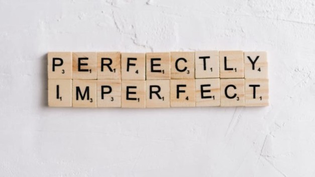 Scrabble tiles on white surface spell 'Perfectly Imperfect' with ample copy space.